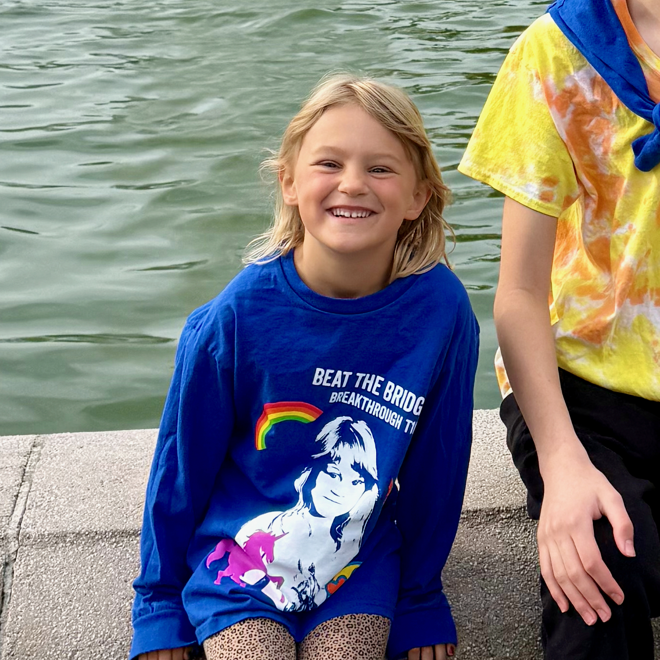 Abigail by the water in her blue Beat the Bridge for Breakthrough T1D t-shirt, smiling