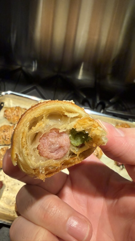 Cross-section showing flaky puff pastry layers around sausage and cornichon